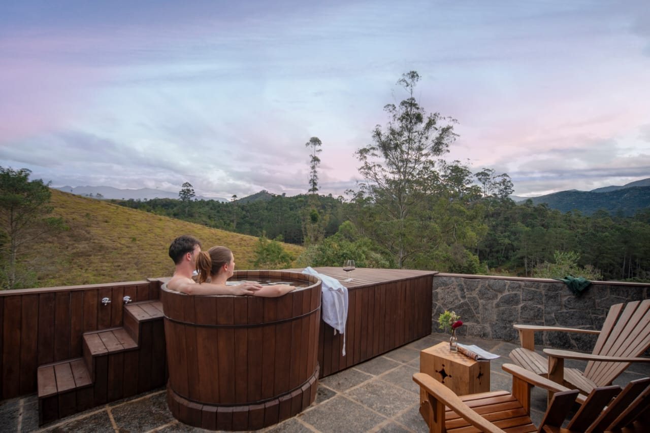 Casal no ofurô externo do Chalé Superior Terras Altas, com a serra ao fundo no fim da tarde